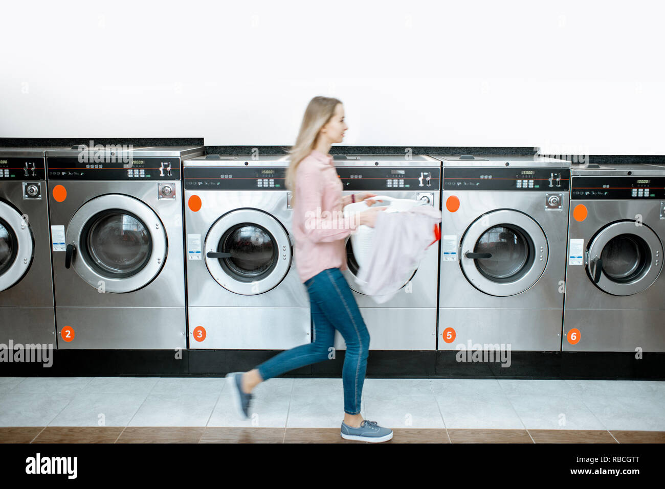 Woman walking with clothes at the self service laundry with washing machines on the background, motion blurred woman Stock Photo