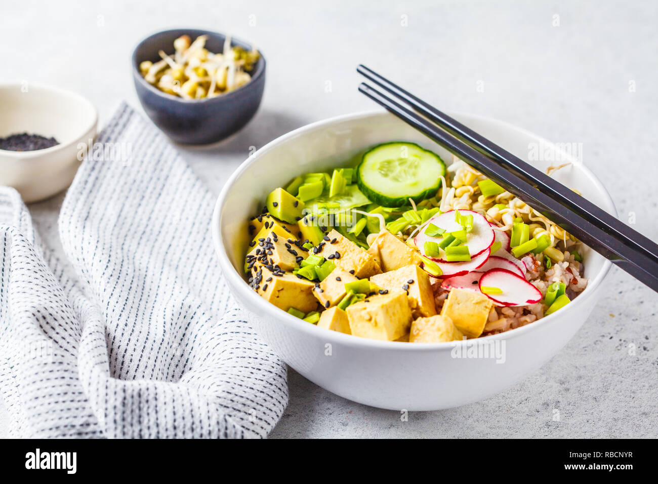 Vegan poke bowl with pickled tofu, vegetables and rice in a white bowl. Plant based diet concept. Stock Photo