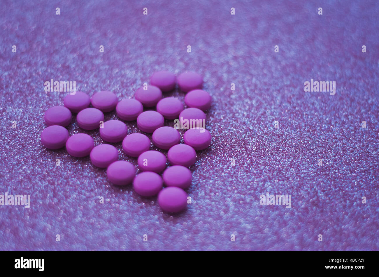pink pills laid out in shape of a heart on glitter pink background