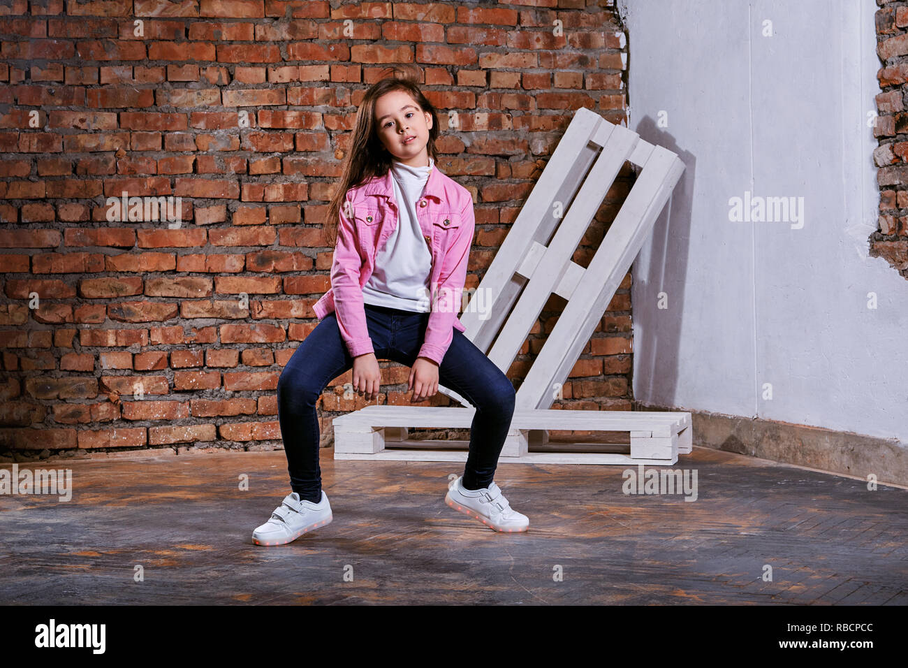 Girl teenager pose movement dance in loft indoors. Beautiful child brunette advertises casual clothes, youth style.Young kid hipster 9-13 years in pink jacket denim, jeans, sneakers. Stock Photo