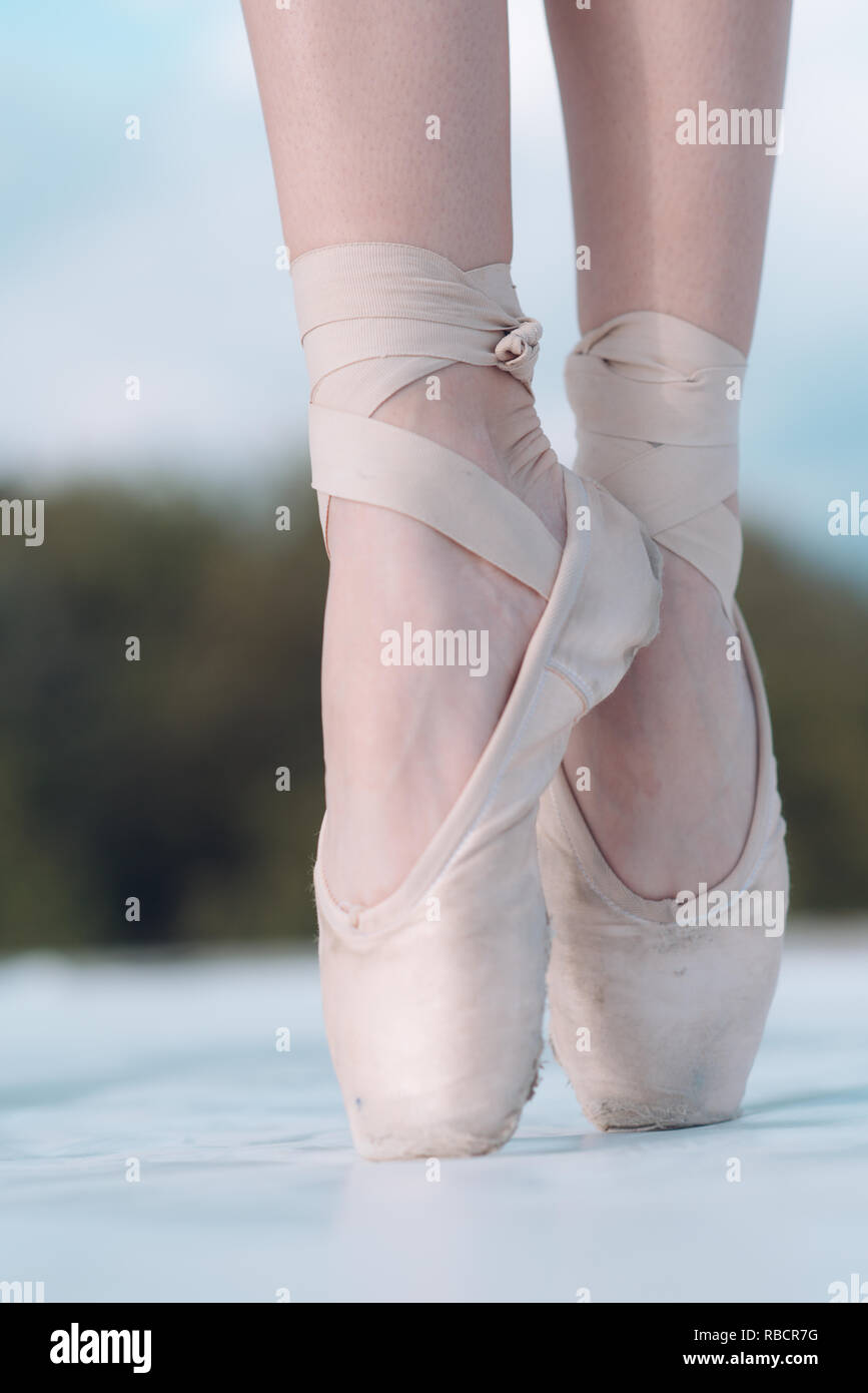On the tips of the toes. Female feet in pointe shoes. Pointe shoes worn by ballet dancer. Ballerina shoes. Legs in white ballet shoes. Ballet slippers. Classic dance style. Dance performance Stock Photo