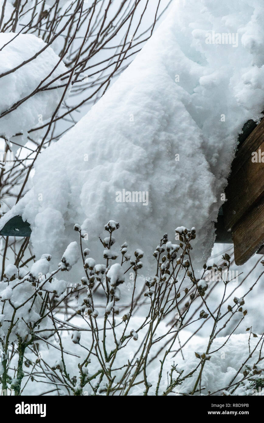 Snow drift on roof after two days of snowfalls. Thick layers hanging on the house roof. Germany Bavaria Stock Photo