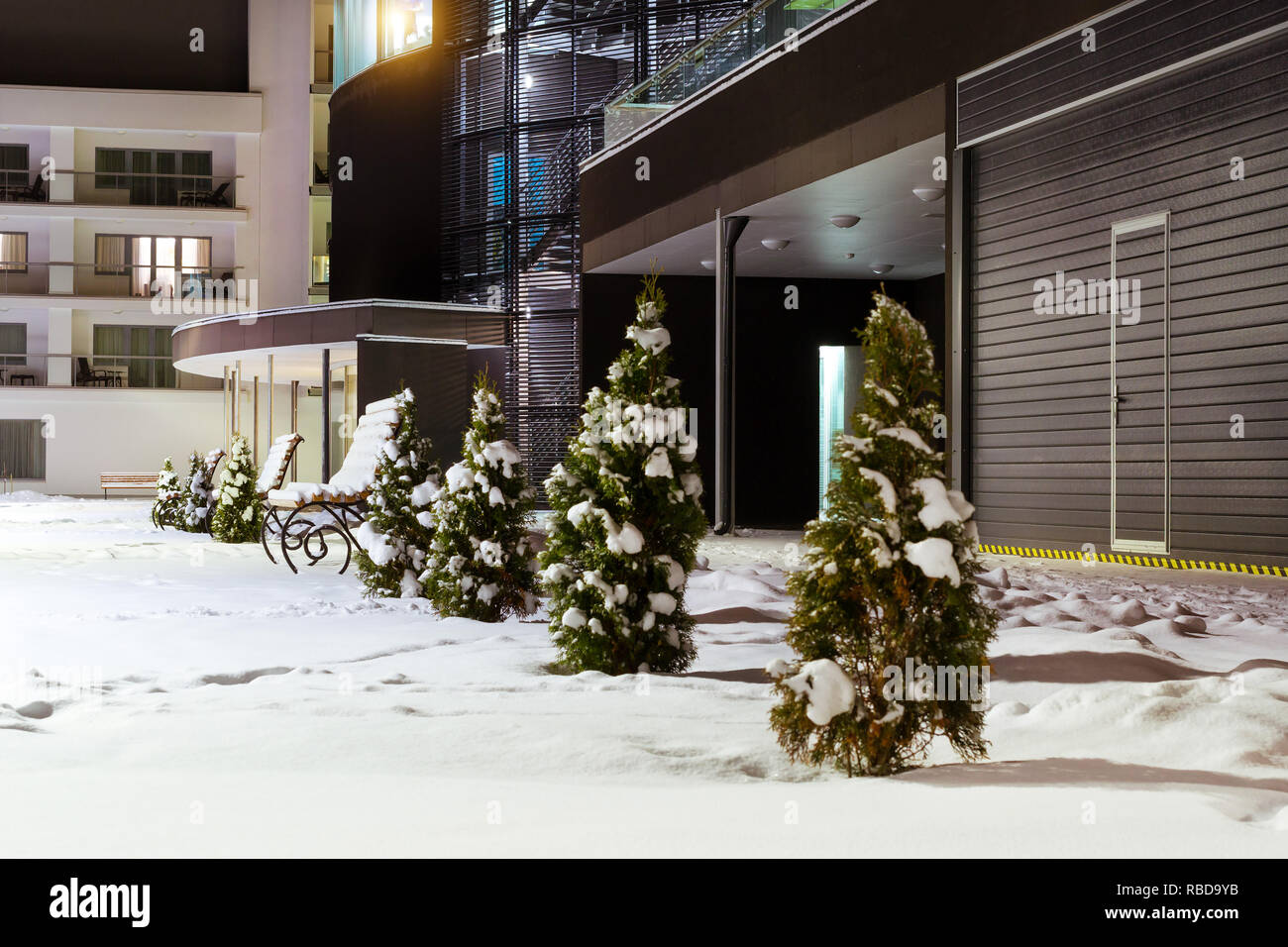 Modern building made of glass and concrete amidst snowy winter landscape at night. Severe Northern winter and snowy weather. Snow-covered wooden benches. Narva-Joesuu Stock Photo