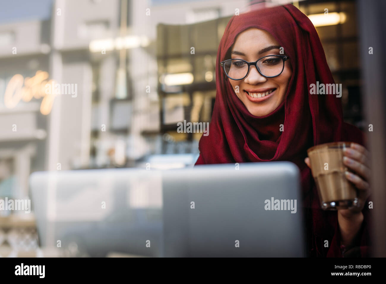 Smiling muslim woman working on laptop at coffee shop. Female in hijab ...