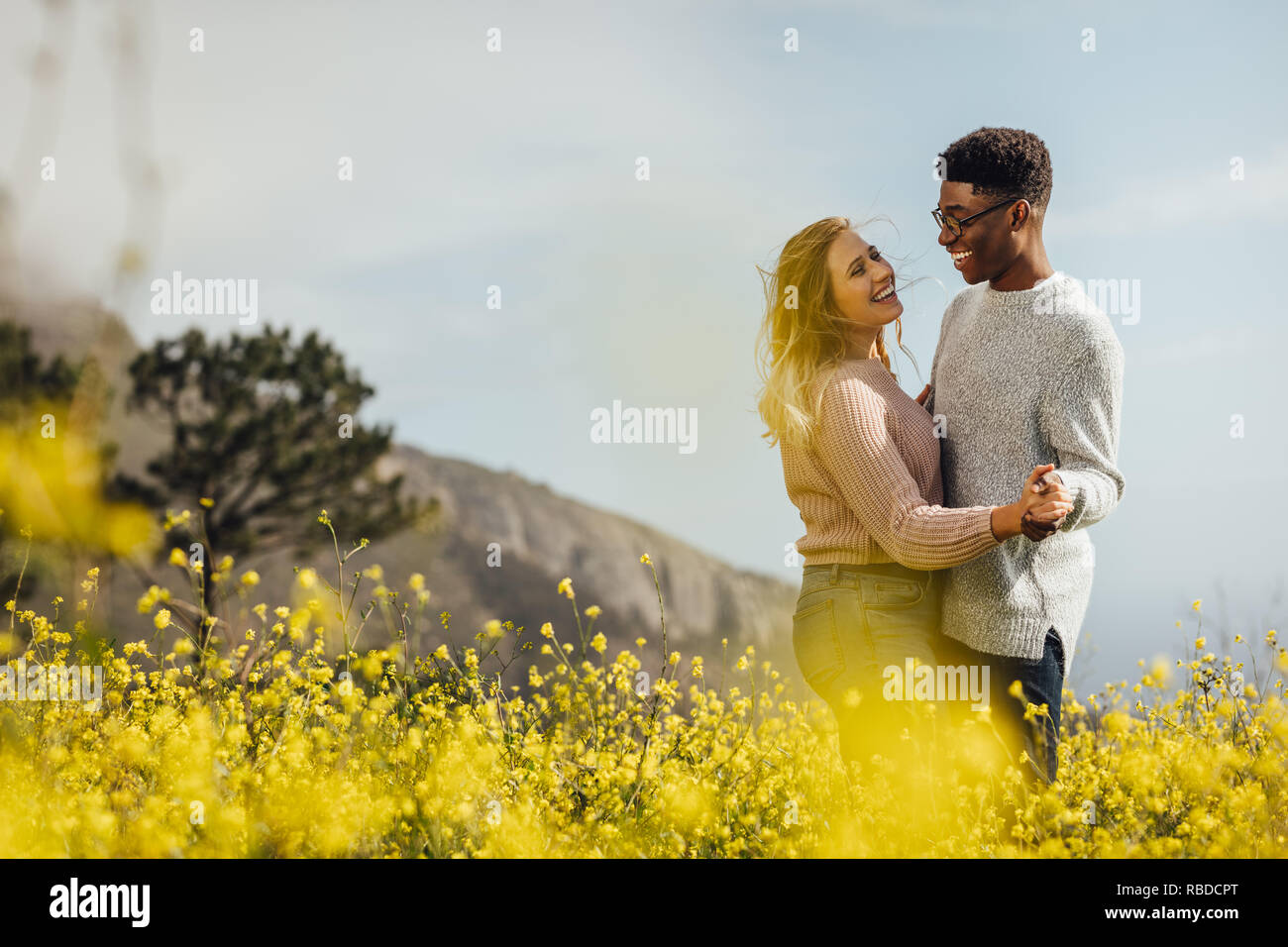 Happy young man and woman dancing outdoors. Couple in love dancing in meadow of yellow flowers. Stock Photo
