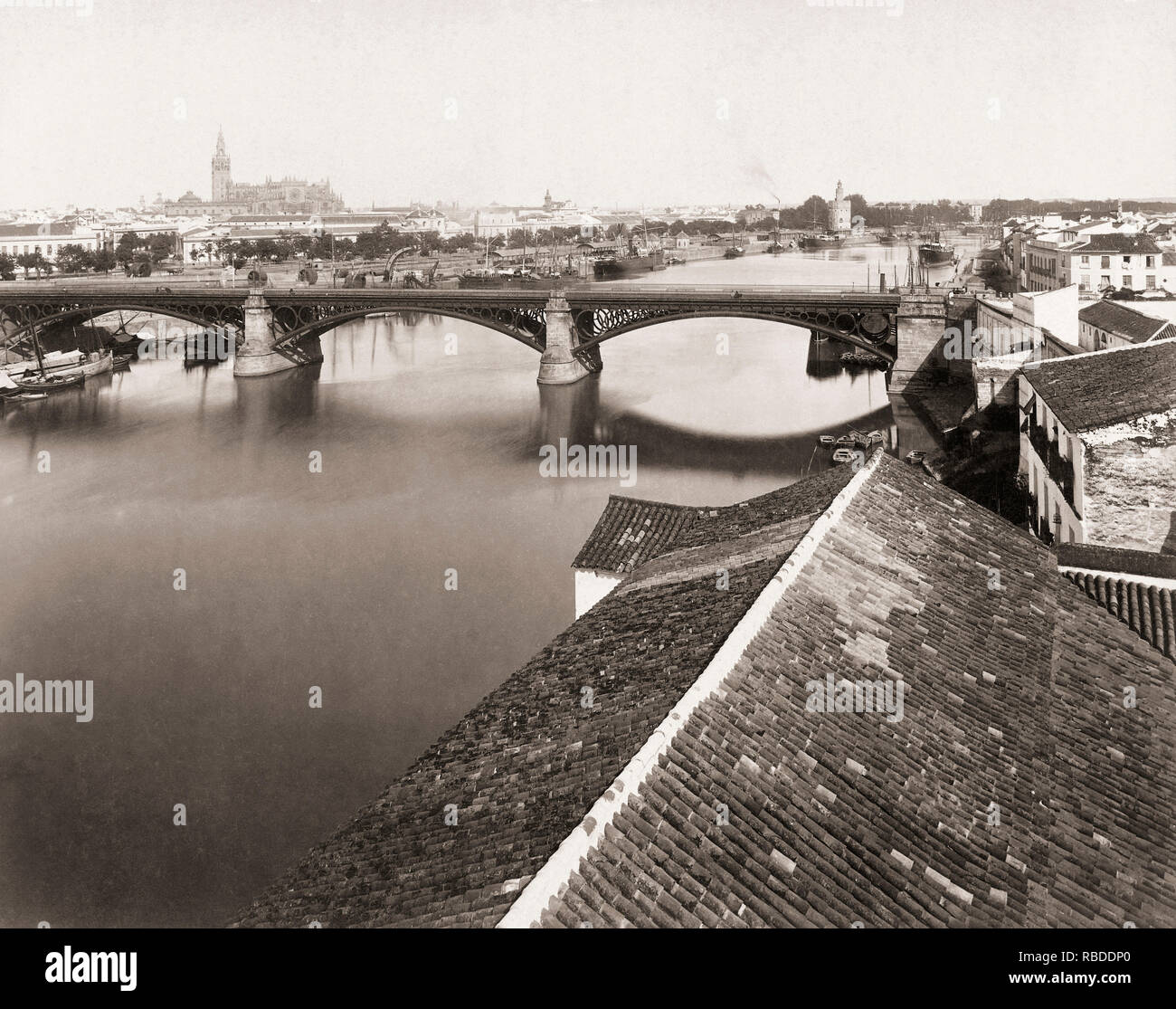 Seville, Seville Province, Andalusia, Spain circa 1880. The Guadalquivir River.  In the mid-distance is the Triana Bridge.  The Cathedral with the Giralda Tower can be seen in the background, left, and the Torre de Oro, or Tower of Gold, to the right.  From a 19th century photograph. Stock Photo