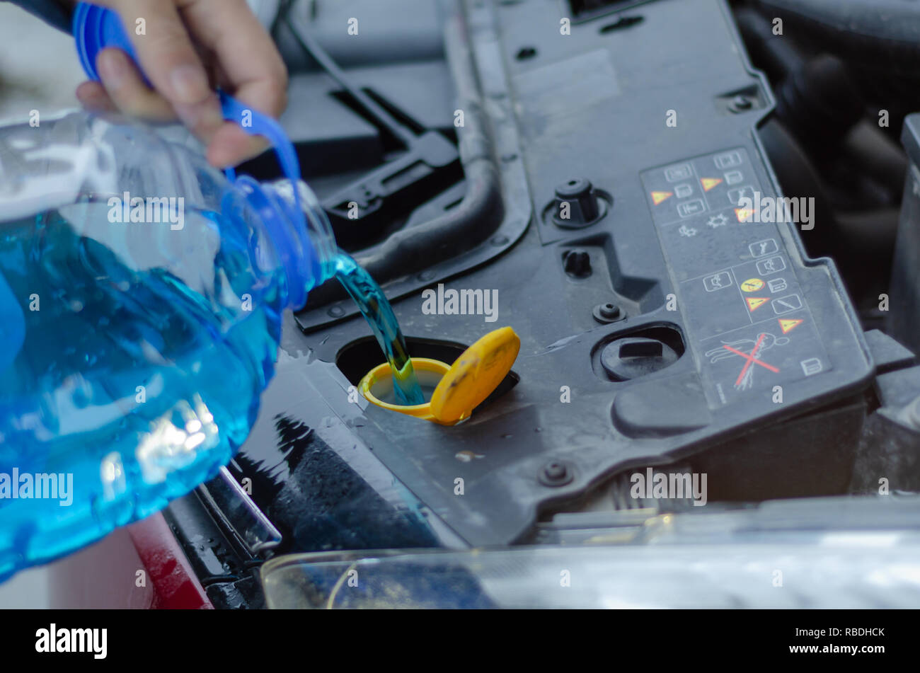 Male is holding  bottle of blue antifreeze in hands and pouring antifreeze liquid for washing car screen. Stock Photo