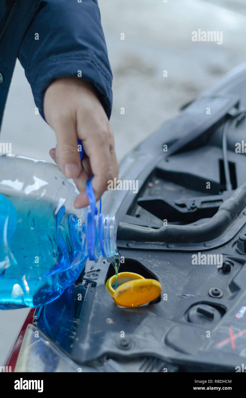 Male is holding  bottle of blue antifreeze in hands and pouring antifreeze liquid for washing car screen. Stock Photo
