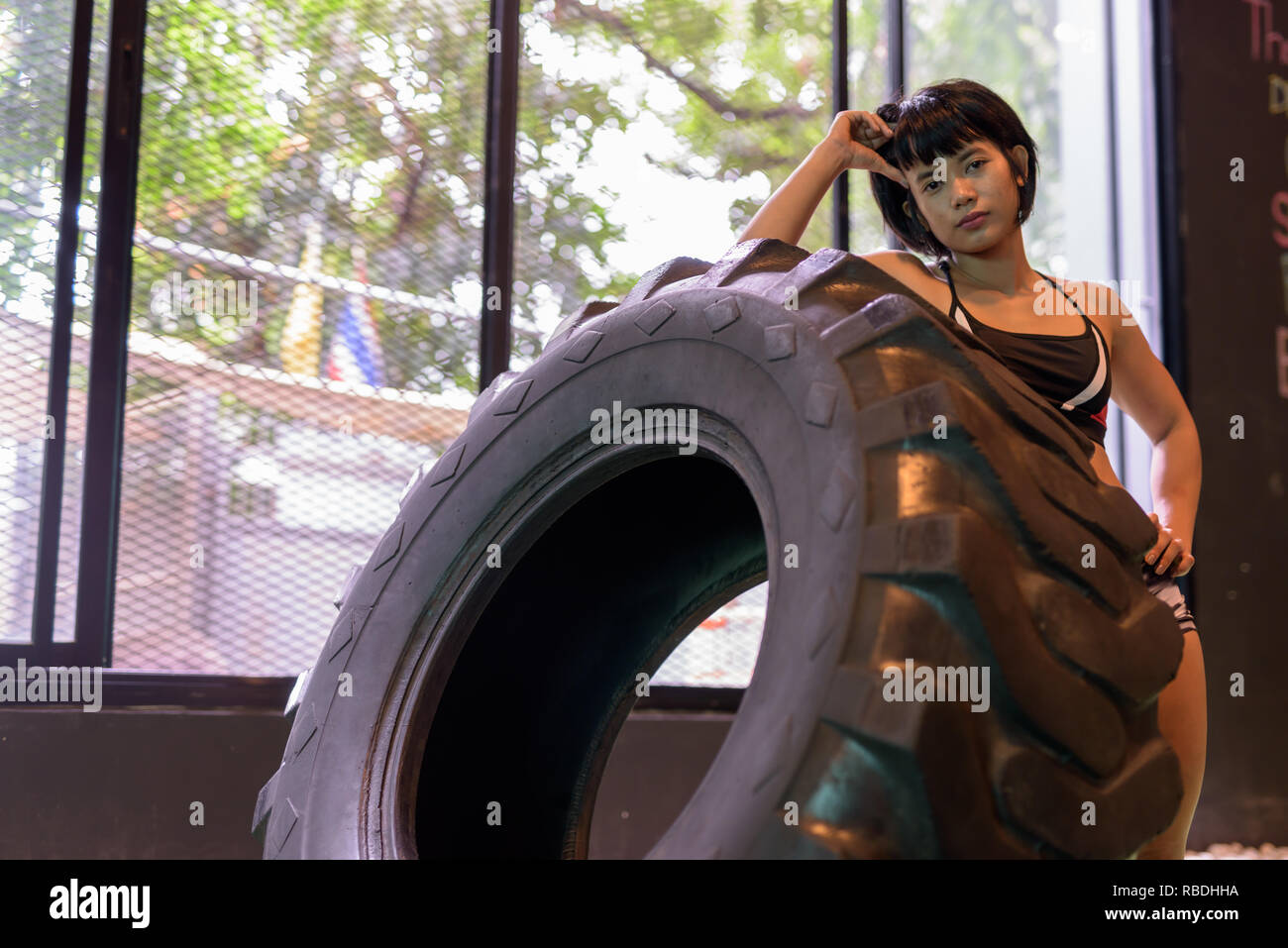 Asian fitness woman pushing and flipping wheel truck tire at gym Stock Photo