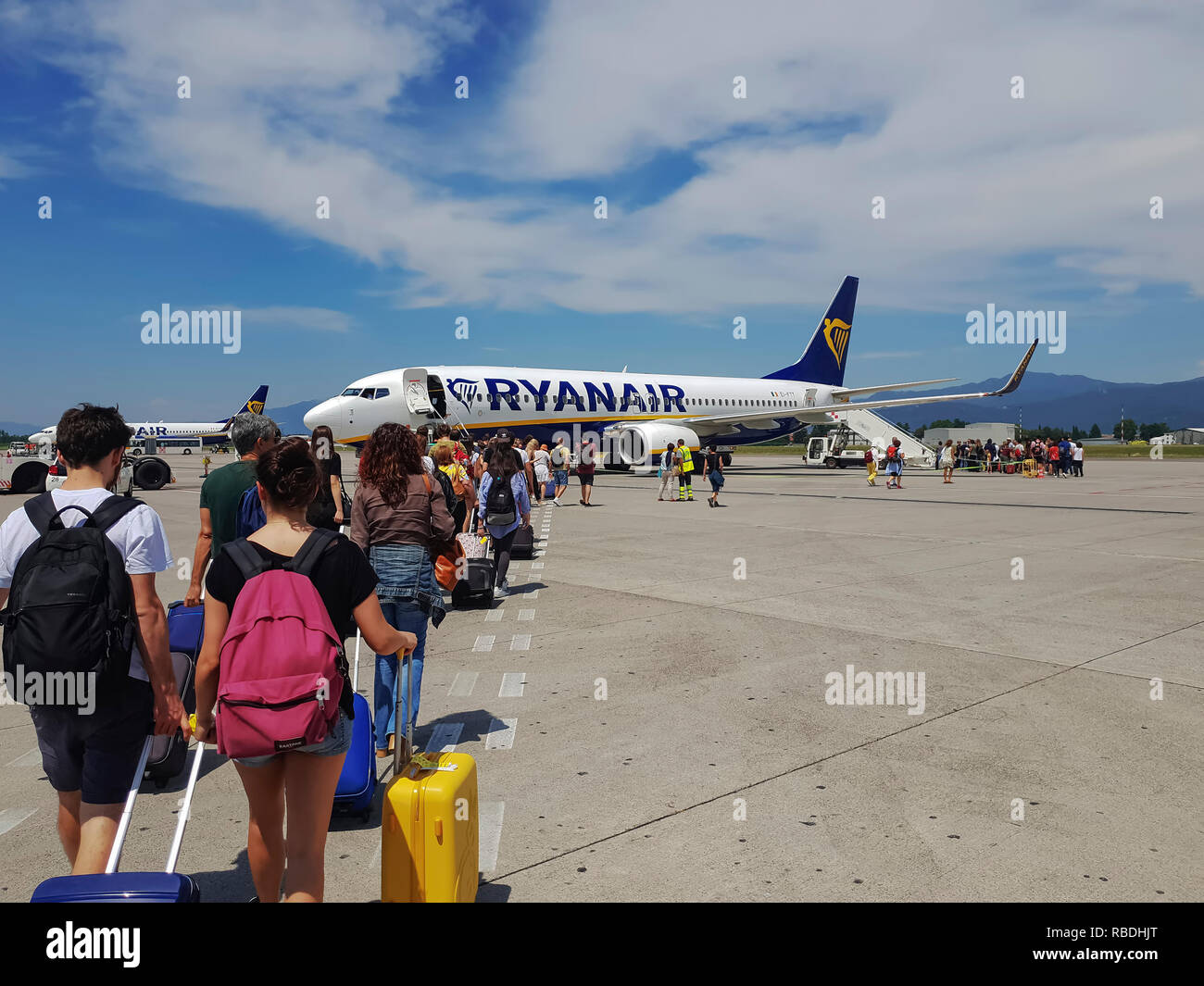 Passengers walking on tarmac of Milan Bergamo Airport. Travelers with luggage at apron area of Orio al Serio airport ready to board a Ryanair aircraft Stock Photo