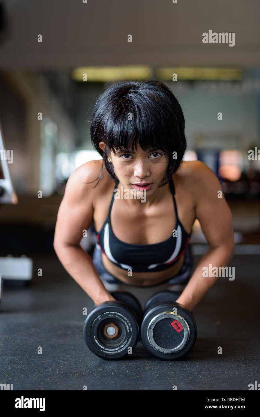 Fitness woman doing plank with dumbbells in gym Stock Photo