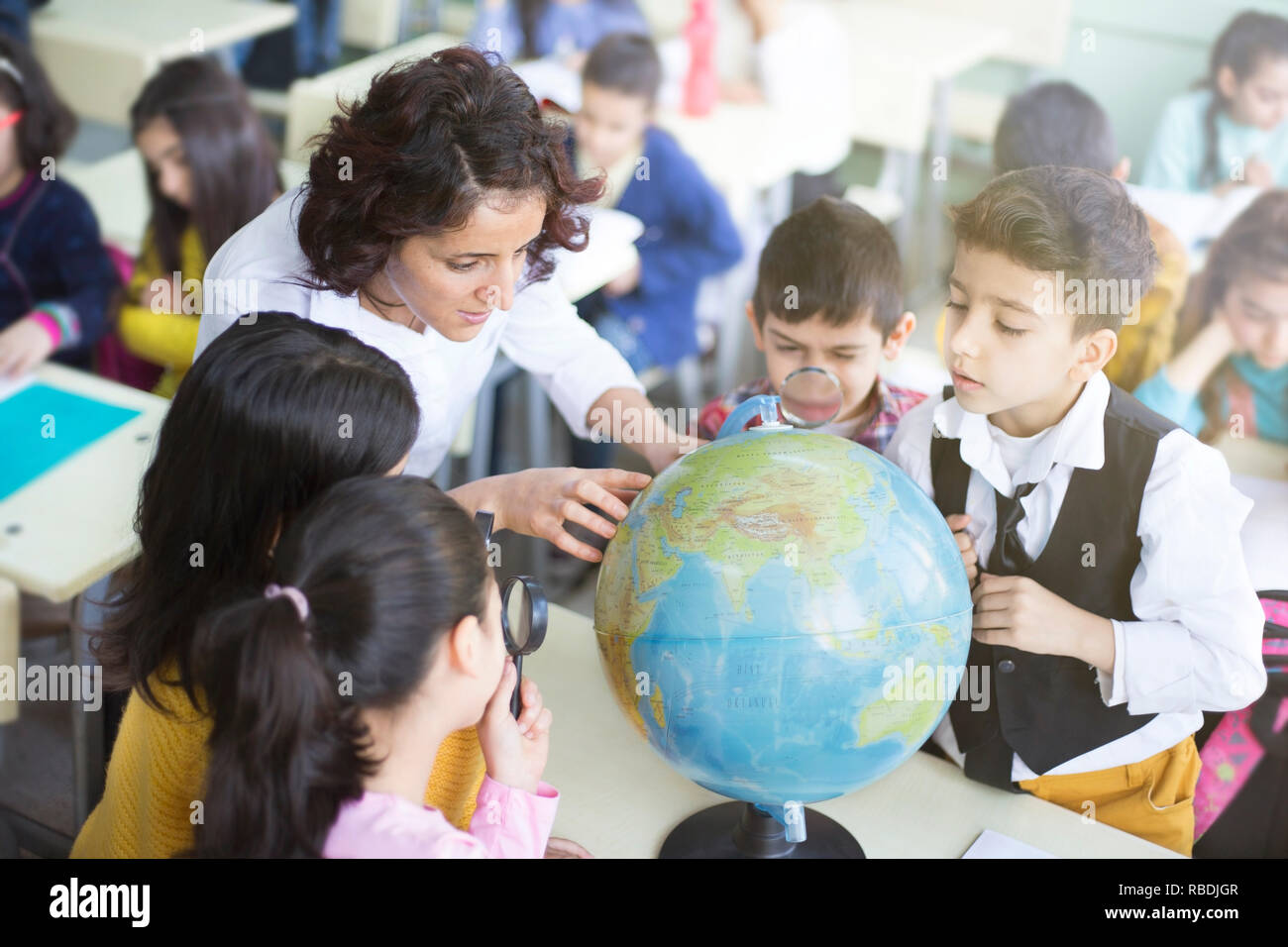 female teacher and students looking the globe with a magnifying glass in the classroom Stock