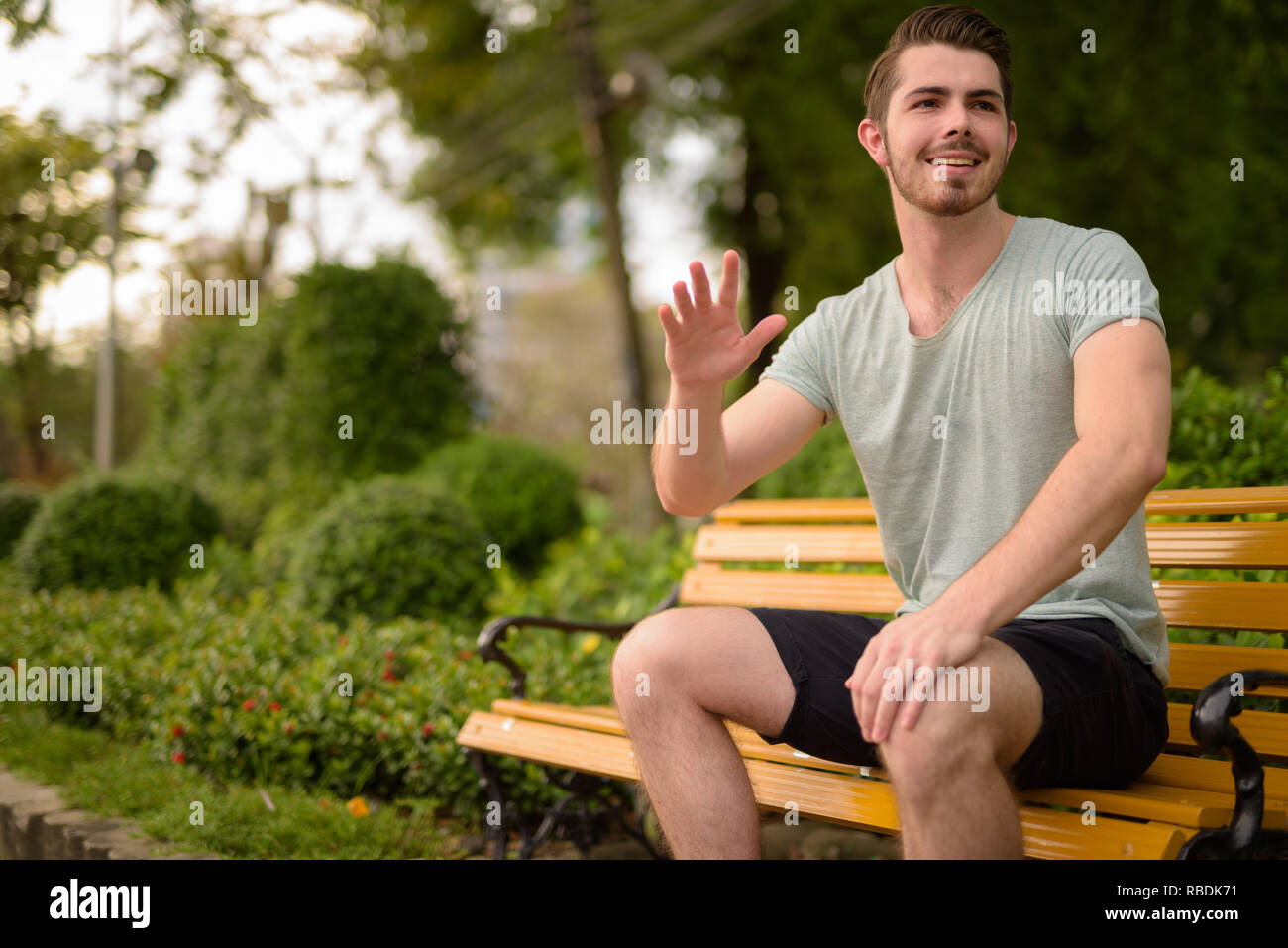 Portrait of young handsome man sitting at park while greeting Stock Photo