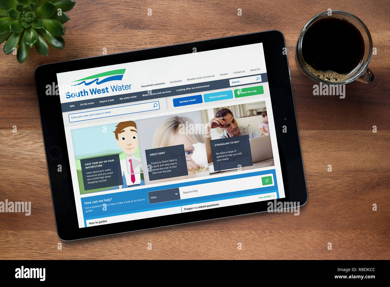 The website of South West Water is seen on an iPad tablet, on a wooden table along with an espresso coffee and a house plant (Editorial use only). Stock Photo