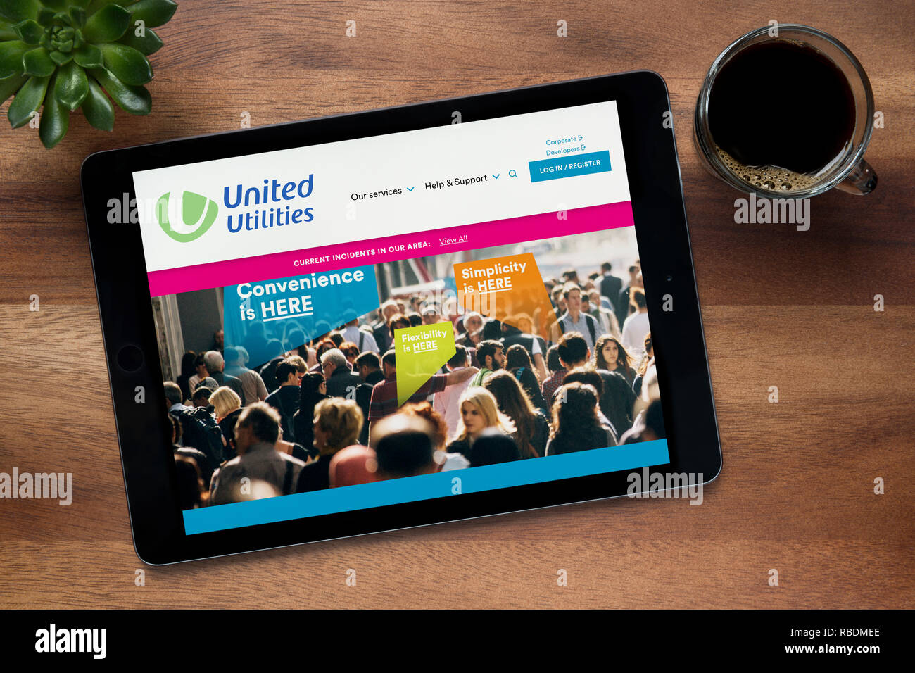 The website of United Utilities is seen on an iPad tablet, on a wooden table along with an espresso coffee and a house plant (Editorial use only). Stock Photo