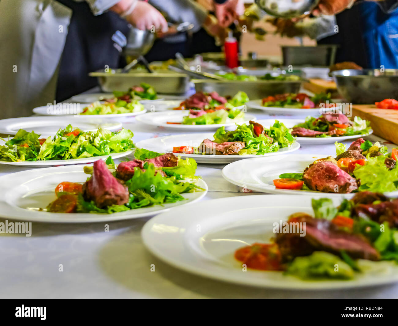 Cooked Roast Beef, Fresh Salad And Tomatoes Served On White Plates. Cooking Master Class, Workshop with People Learning How to Cook Around the Table Stock Photo