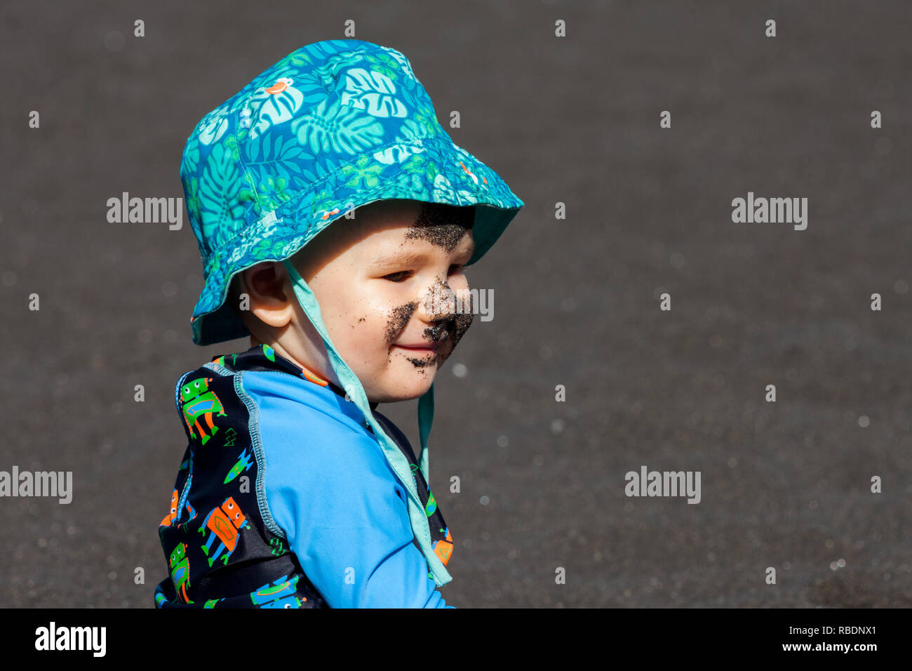 A photo of a nice little boy with a dirty face sitting at the beach Stock Photo