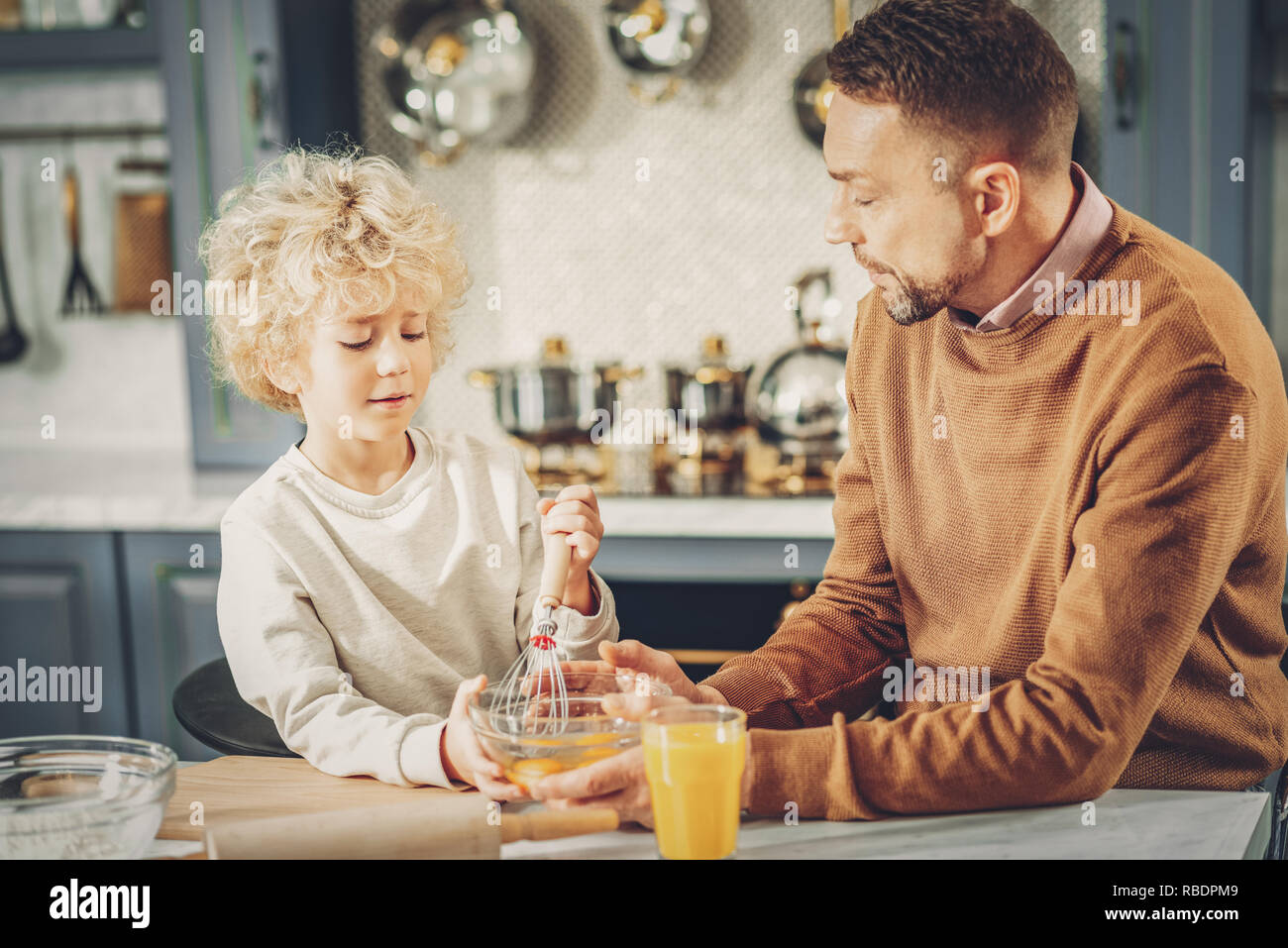 Total concentration. Calm determined man and boy whipping eggs and talking Stock Photo