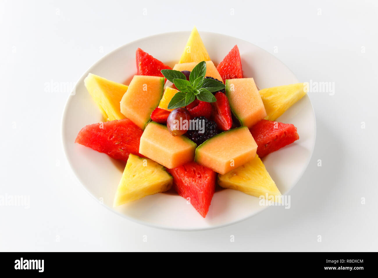 A plate of assorted tropical fruit shaped into a star including watermelon, pineapple, cantaloupe, grapes, blackberries, strawberries, raspberries, an Stock Photo
