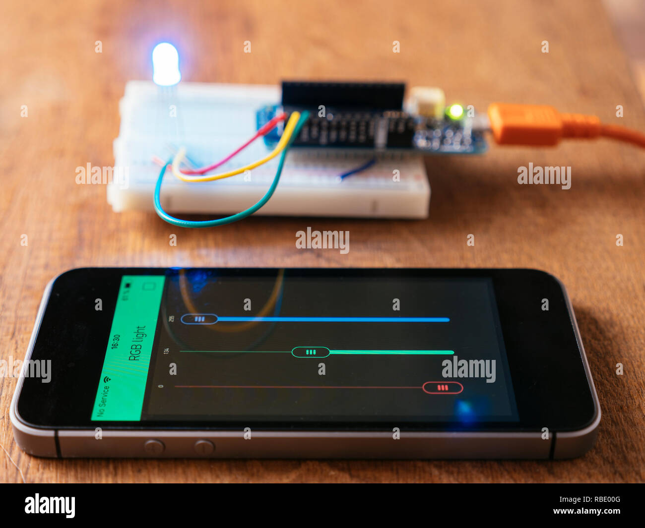 RGB Led on a breadboard with microcontroller board being controlled by a mobile phone app. Stock Photo