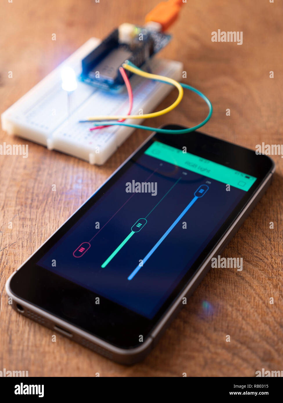 RGB Led on a breadboard with microcontroller board being controlled by a mobile phone app. Stock Photo