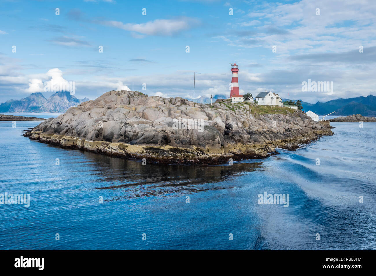 Lighthouse on island Skrova, rocky small island, view towards Lofoten islands, mountain Vagekallen near Henningsvaer in the back, peak covered by clou Stock Photo