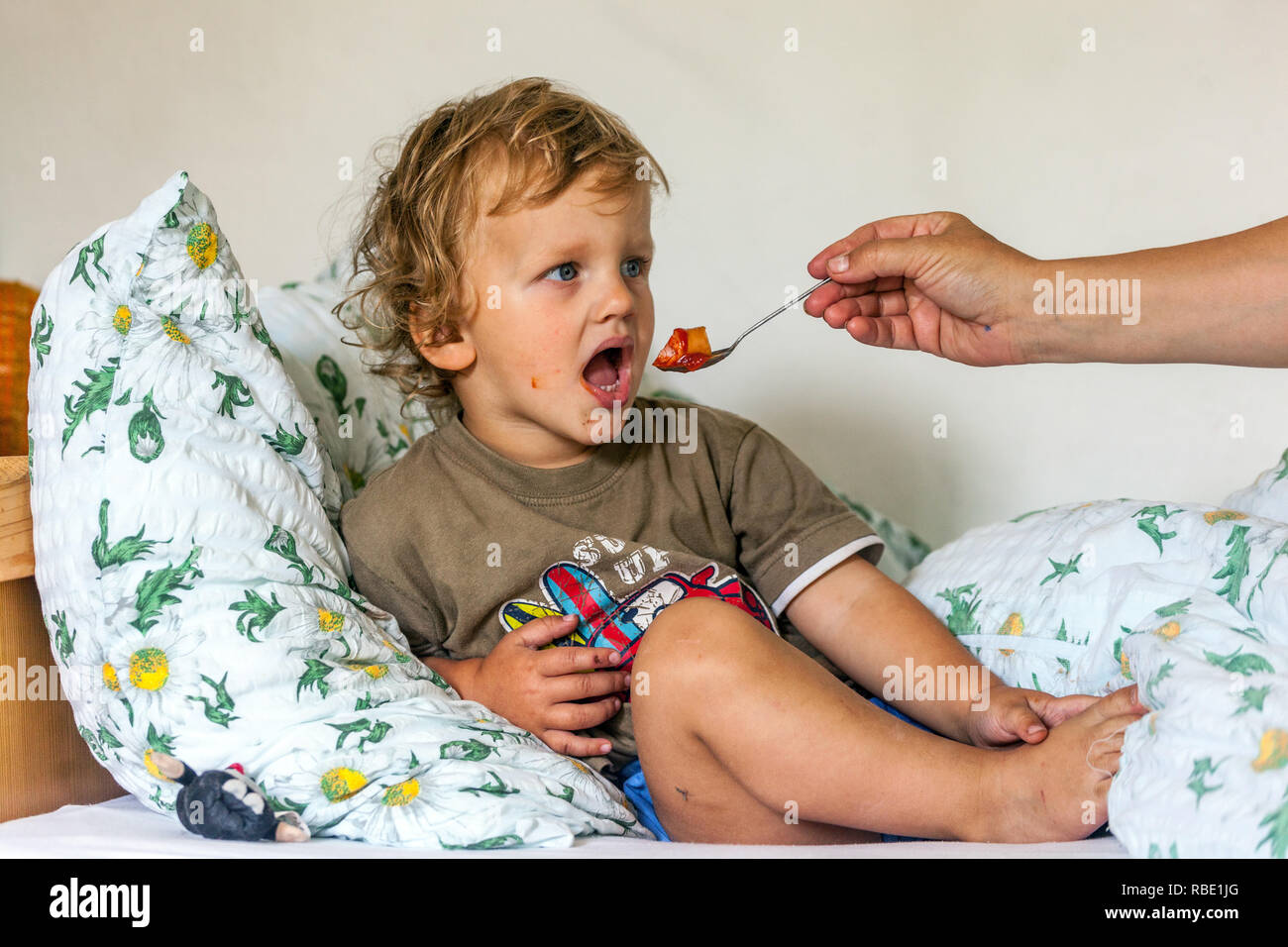 Young boy, toddler eating in bed, spoon feeding child, people feeding people Stock Photo