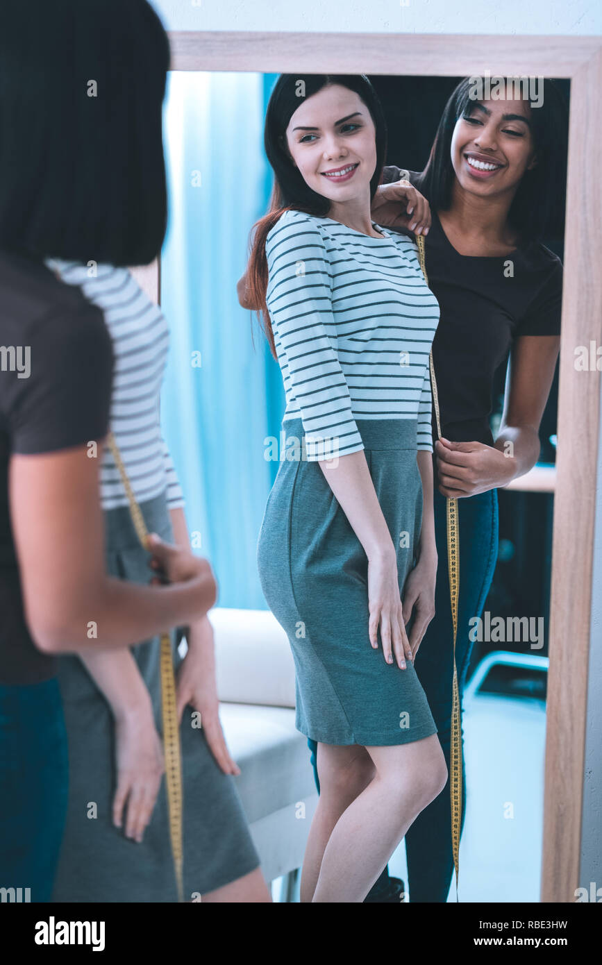 Personal tailor. Popular tailor taking measures from client standing near the mirror Stock Photo
