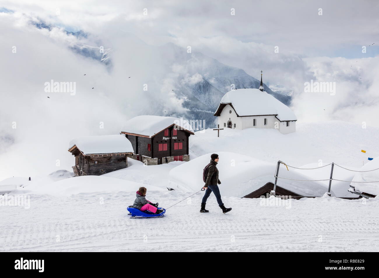 Child on a sledding admires mountain huts covered with snow Bettmeralp district of Raron canton of Valais Switzerland Europe Stock Photo