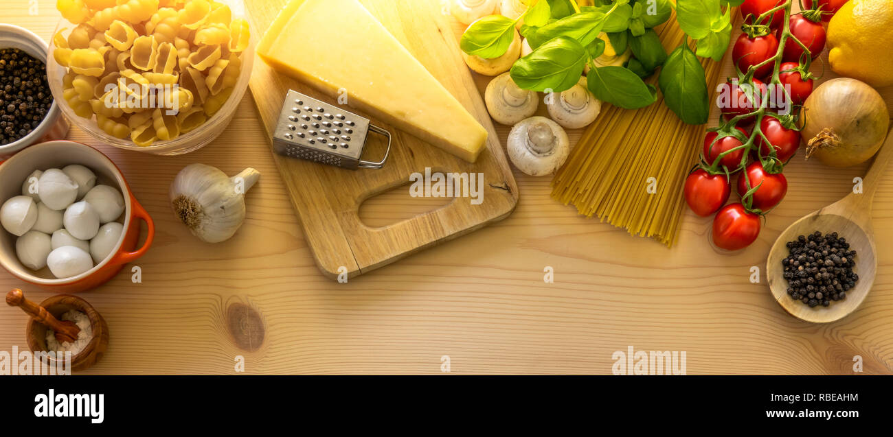 Italian food cooking ingredients. Vegetables, mozzarella cheese, herbs and pasta on wooden background. Stock Photo
