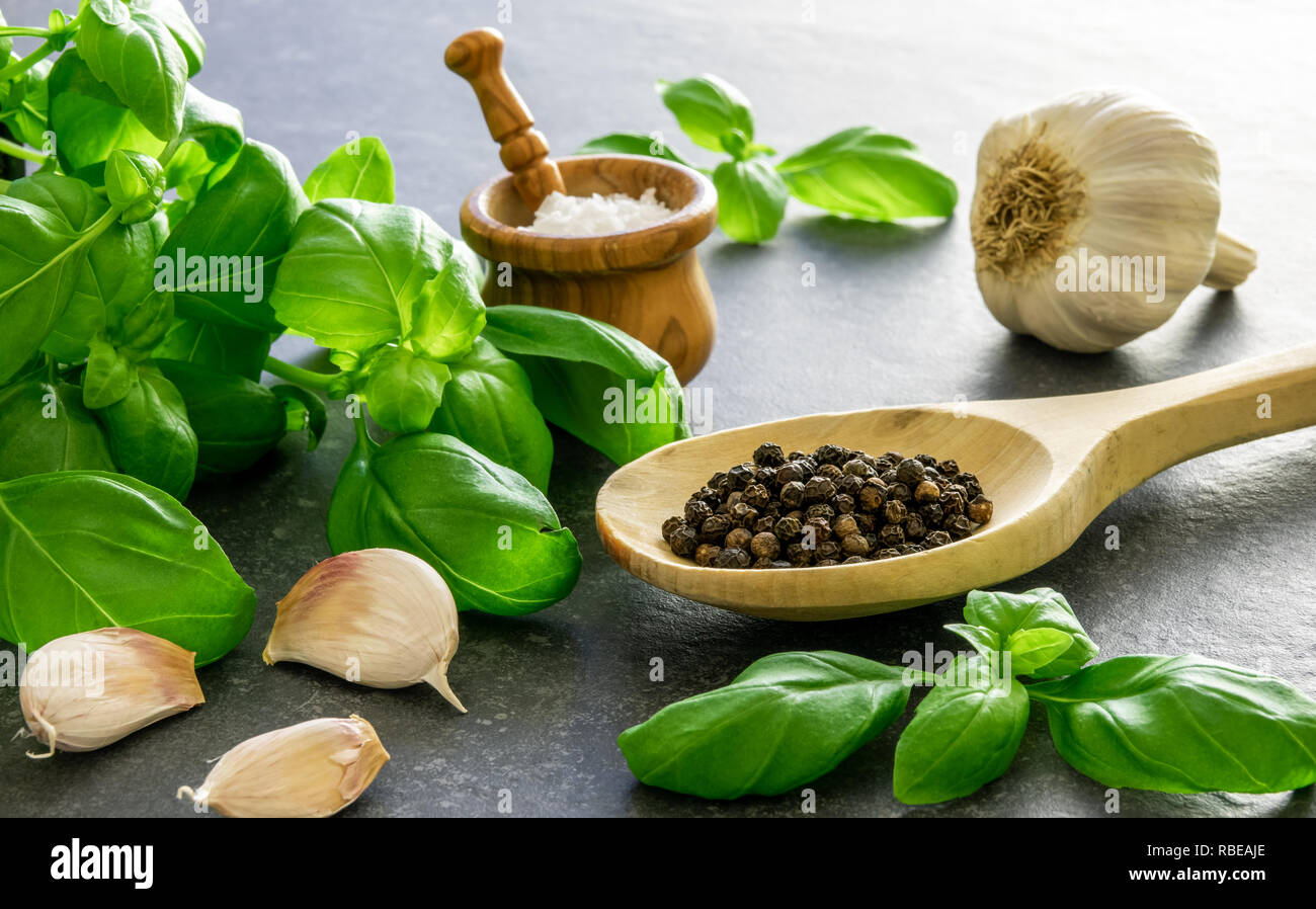 Italian food ingredients. Herbs and seasoning spices. Basil, garlic, salt and pepper on dark stone. Stock Photo