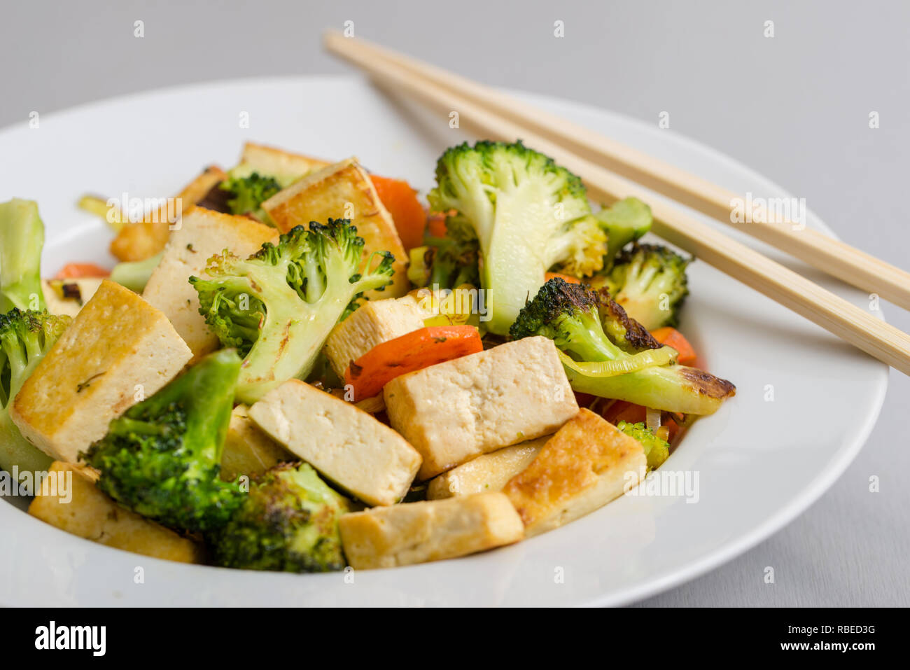Grilled tofu with broccoli and carrots in white plate with chopsticks