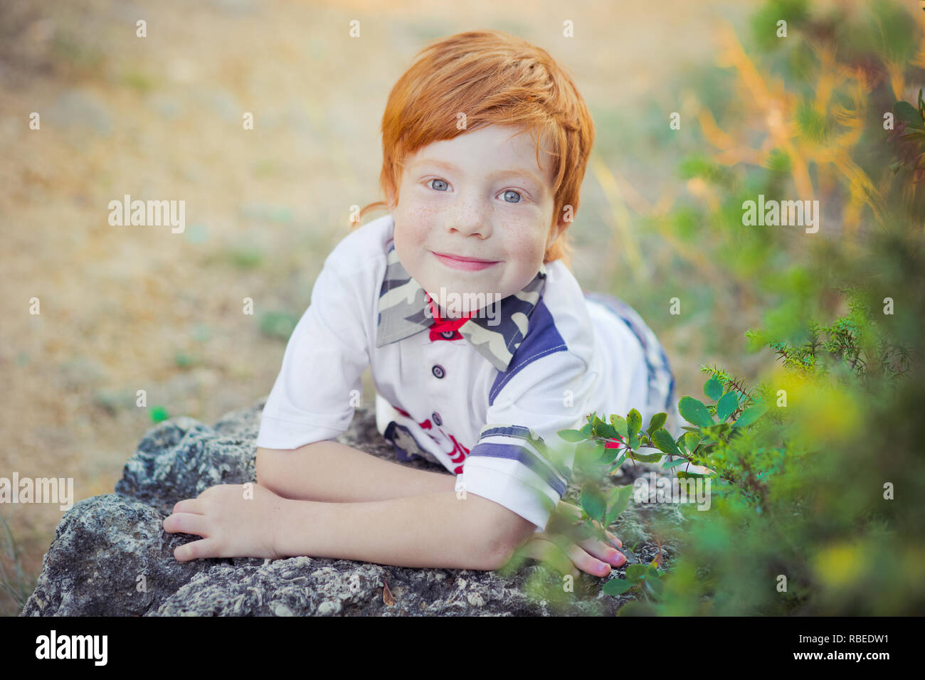 Cute red hair boy smiling to camera and standing in forest Stock Photo