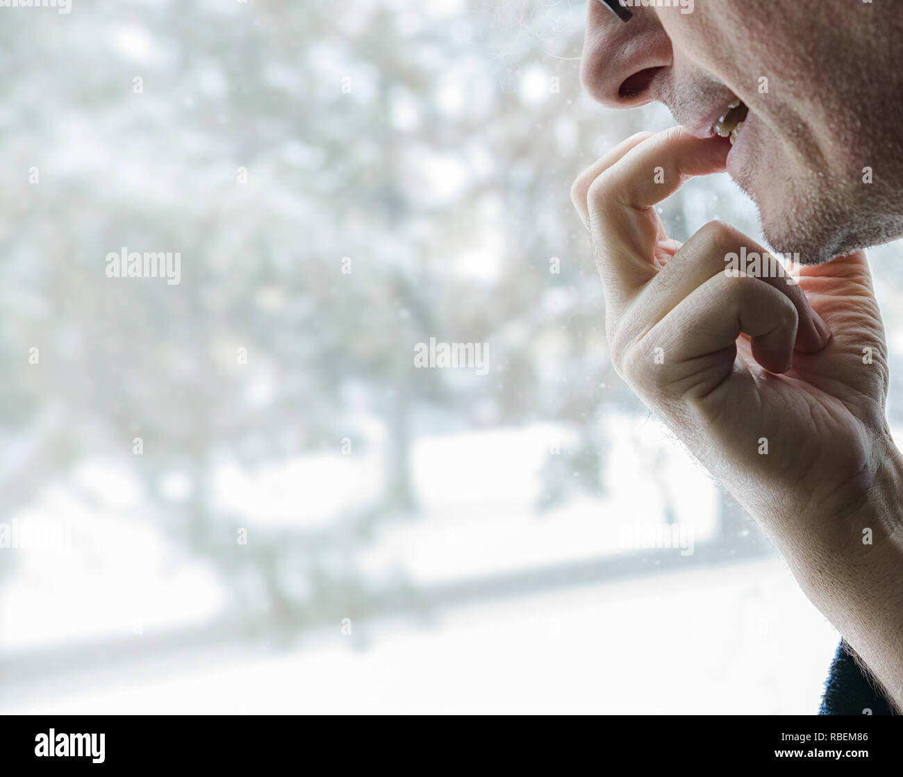 A mature male bites his nails while waiting and looks out the window. Profile view. Stock Photo