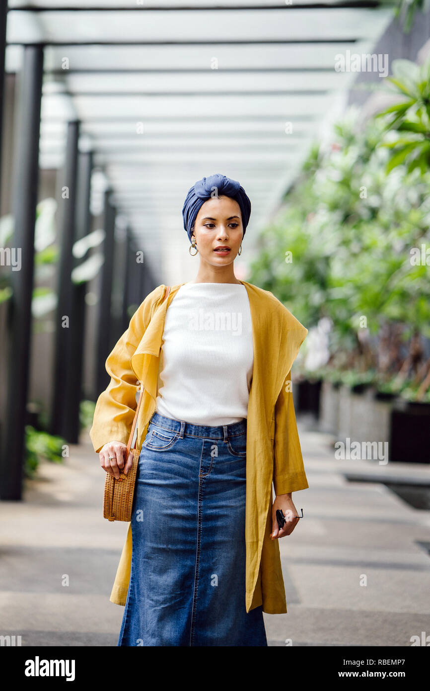 Portrait of a tall, beautiful and elegant Middle Eastern Arab woman in a turban and a pastel outfit standing on a street in the city. Stock Photo