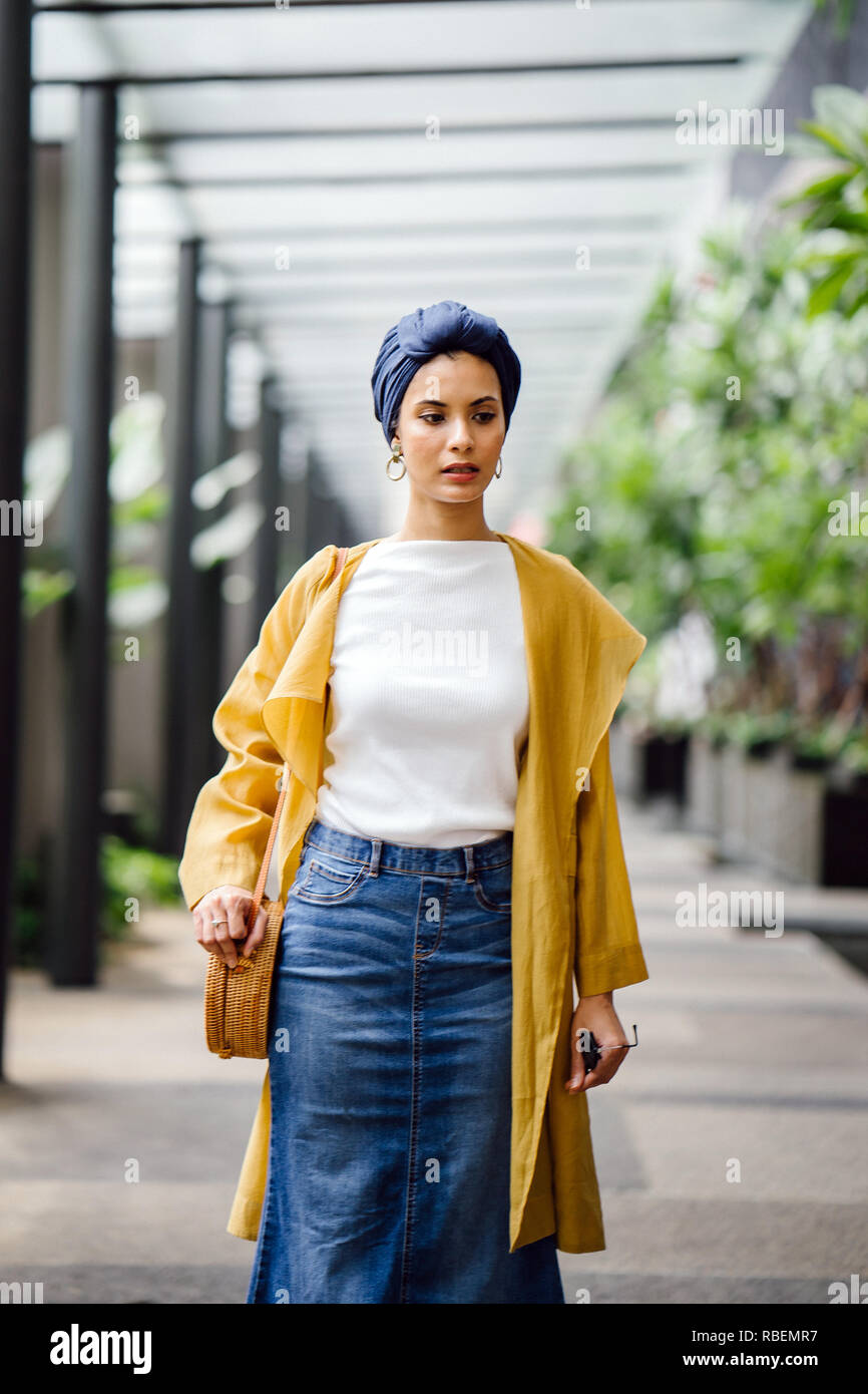 Portrait of a tall, beautiful and elegant Middle Eastern Arab woman in a turban and a pastel outfit standing on a street in the city. Stock Photo