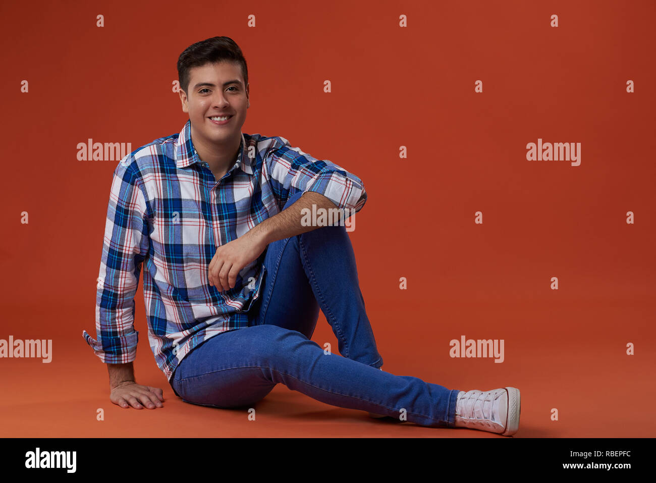 Young man sit on floor in casual outfit isolated on orange color background Stock Photo