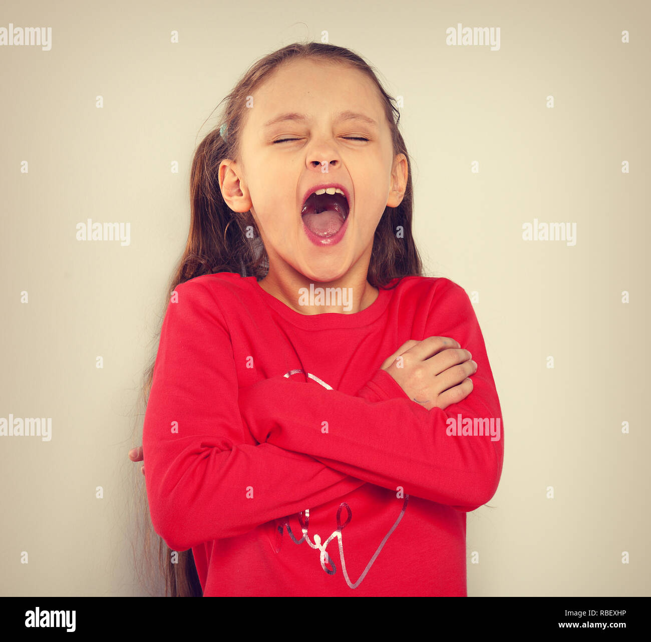Kid girl strong screaming with open mouth and folded arms on toned vintage background with empty copy space Stock Photo