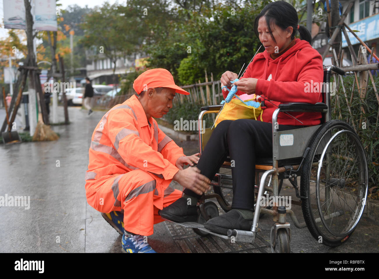 (190110) -- LONGYAN, Jan. 10, 2019 (Xinhua) -- Sanitation worker Dong Jidong helps relax his wife  Dong Jinxiang's legs during work break in Xinluo District of Longyan City, southeast China's Fujian Province, Jan. 9, 2019. Due to femoral head necrosis disease, Dong Jinxiang has been living on a wheelchair for about a decade. To take care of his handicapped wife, Dong Jidong, who himself has been afflicted with ankylosing spondylitis, gave up his work in a cement plant and chose to clean the streets near their home two years ago just in order to take better care of his wife. Everyday, Dong Jido Stock Photo
