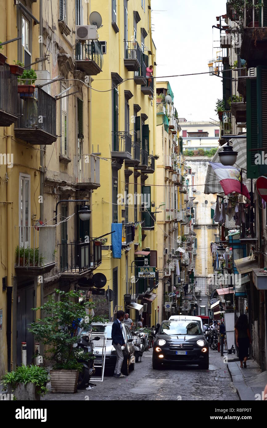 Narrow dark street with cobble stones pavement of historical Naples downtown with typical Mediterranean apartment houses with tiny balconies and woode Stock Photo