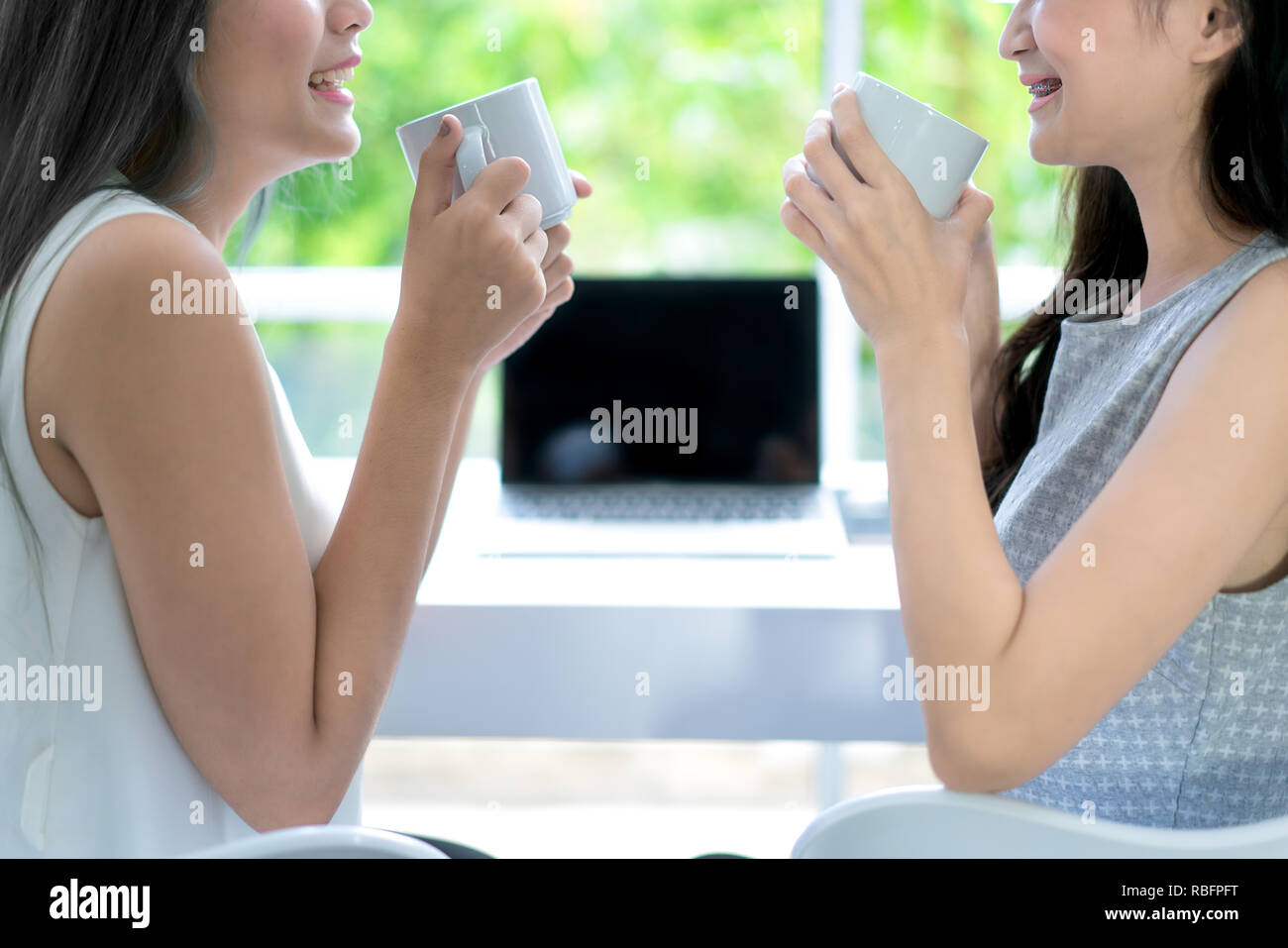 Two young Asian beautiful cheerful woman in sitting on coffee cafe laughing and drinking coffee from a white cups. Stock Photo