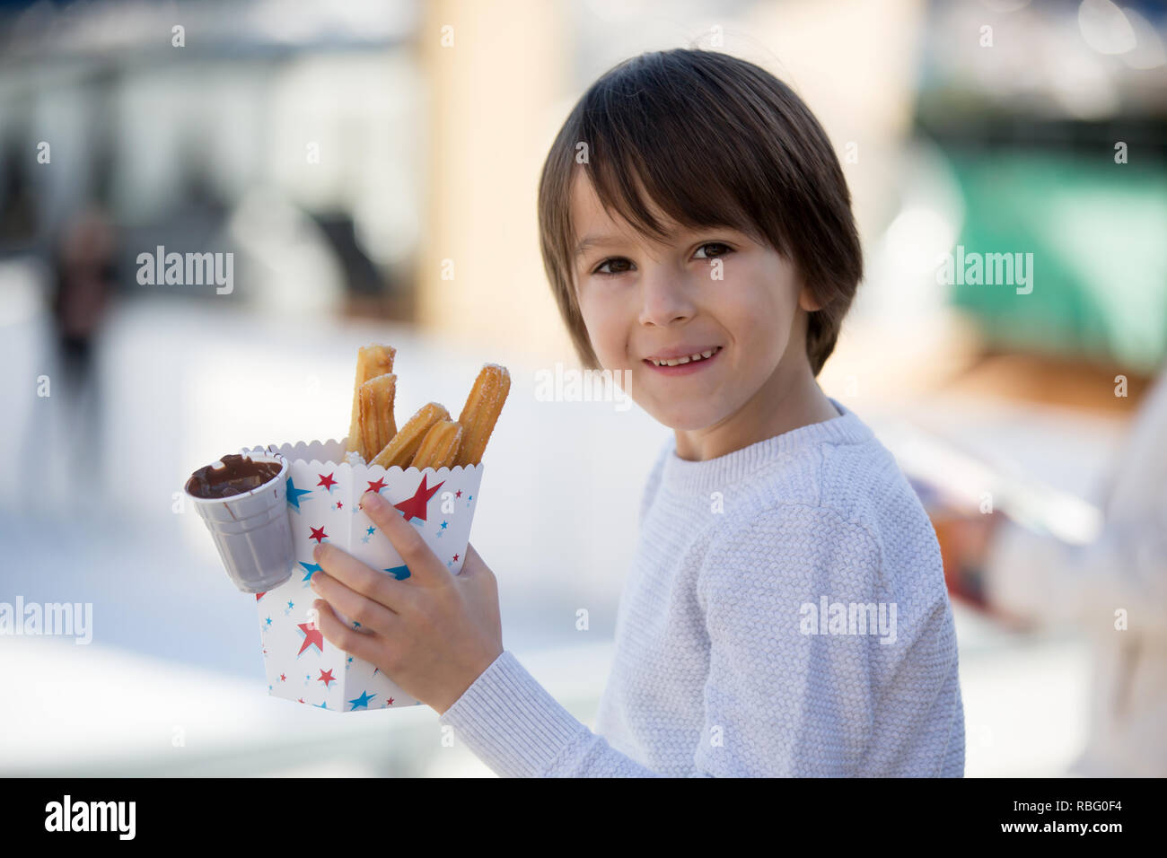 Kid eating churros. Sweet Fried Custard Dough Pastry in bag with chocolate in boy's hands