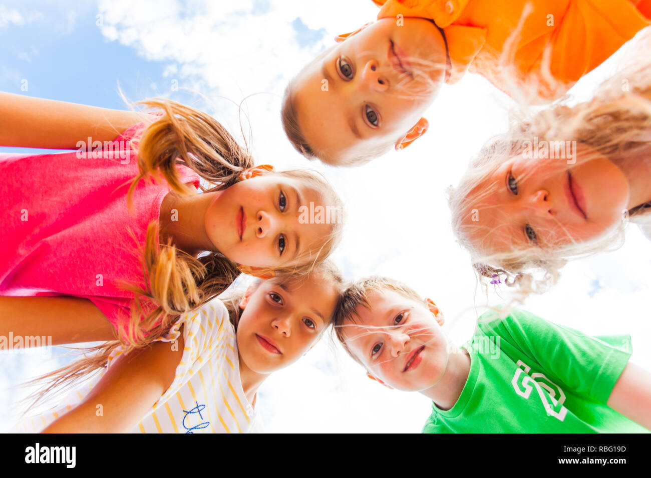 Five happy kids standing leaning upon the camera looking at it. Lovely kids looking at the camera with live ineterest in their eyes. Upward shot Stock Photo