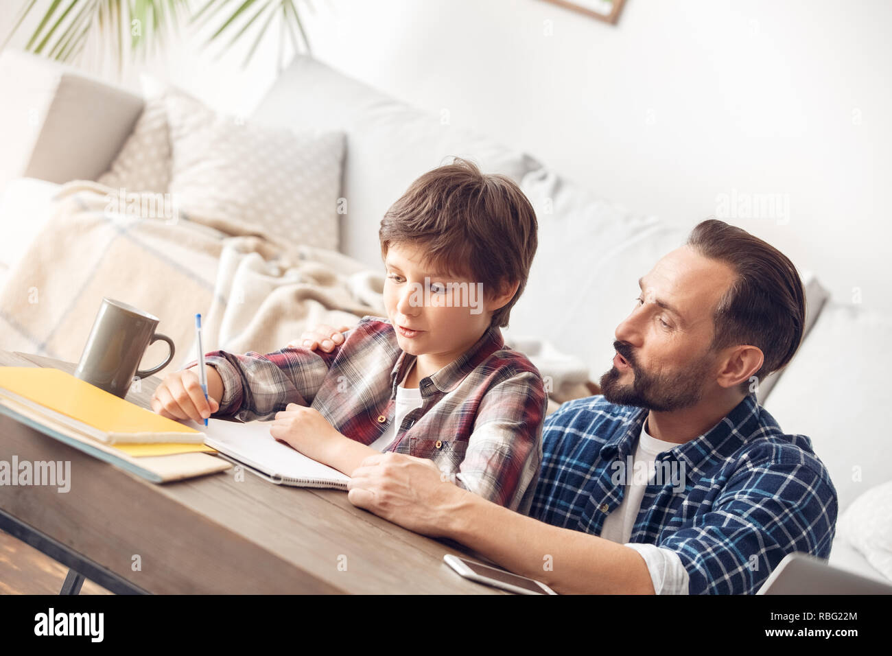 Father and little son together at home sitting at table dad helping boy writing homewrok pronouncing words Stock Photo