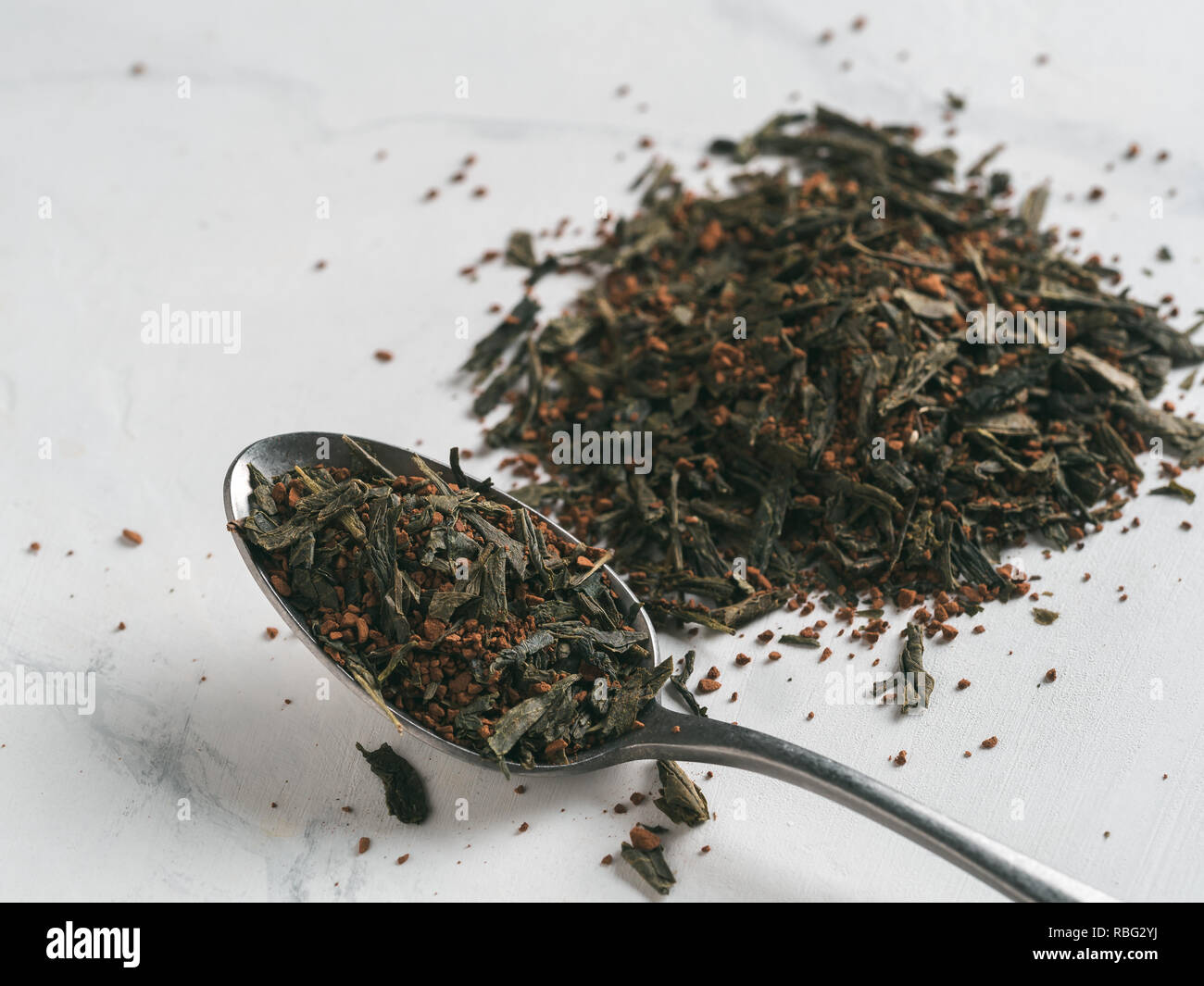Trendy drink idea: Tea-Coffee Blend Combines Two Popular Drinks. Heap of dry mix of green tea and ground roasted coffee beans. Close up view. White marble tabletop. Stock Photo