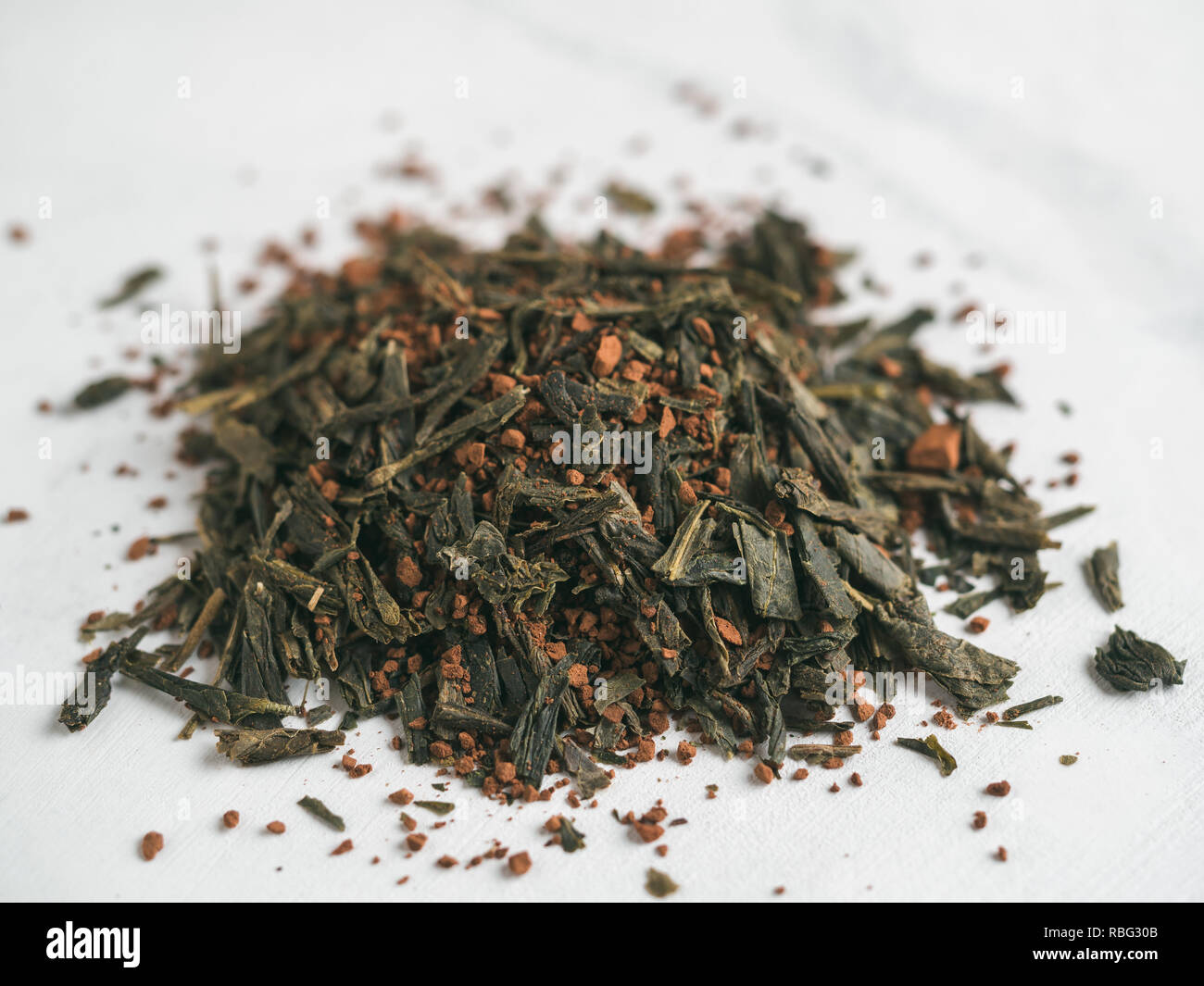 Trendy drink idea: Tea-Coffee Blend Combines Two Popular Drinks. Heap of dry mix of green tea and ground roasted coffee beans. Close up view. White marble tabletop. Stock Photo