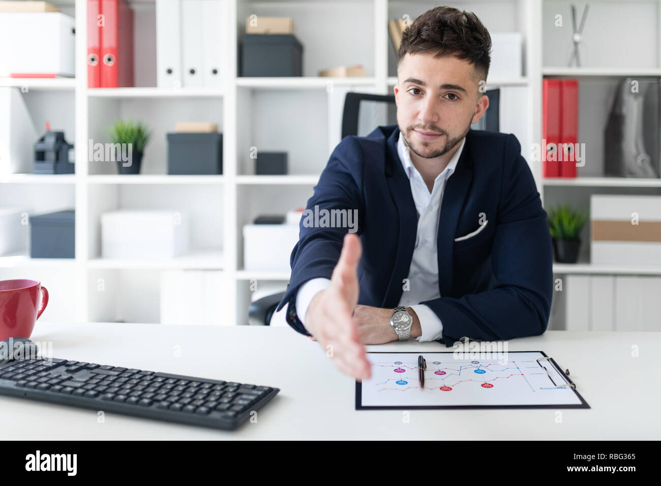 A young man sitting in the office at the computer table and stretches ...