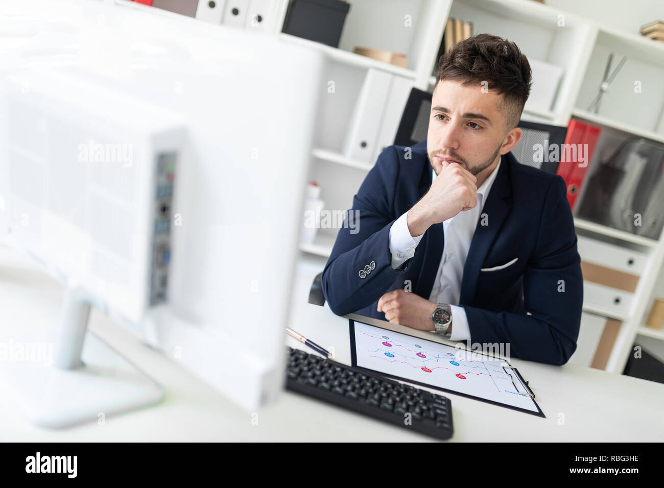 Man At Computer Desk A young man sitting in the office at a computer Desk and working with ...
