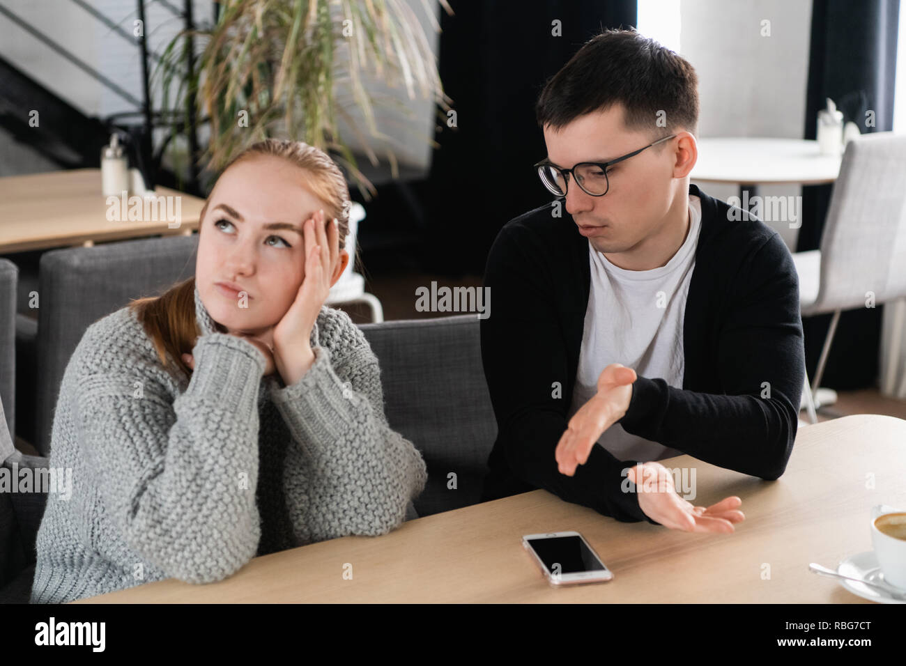 Annoyed man trying to explain something to his wife sitting on a couch in the cafe Stock Photo