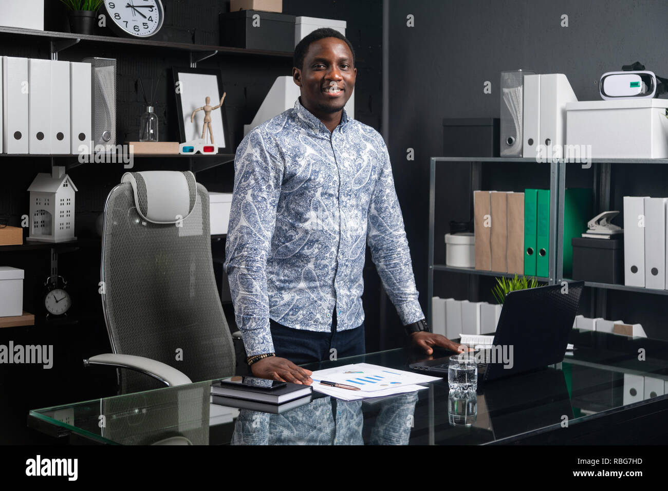 portrait of three-quarters long young black businessman standing near Desk in office Stock Photo